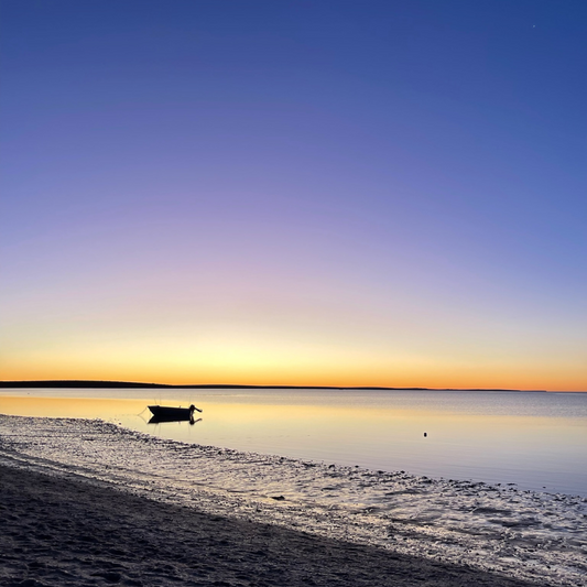 a purple and organge sunset over the ocean with a silhouette of a small boat