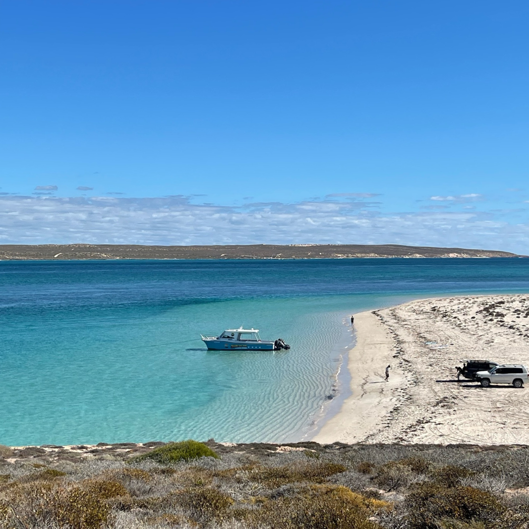 a medium size fishing boat in crystal clear blue water out from an island