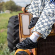 A child wearing black velcro toddler shoes with white socks, sitting on the front of a rusted orange tractor in a grassy field.