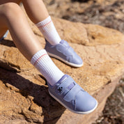 A child wearing light blue slip-on shoes and white crew socks sits on a large tan rock outdoors.
